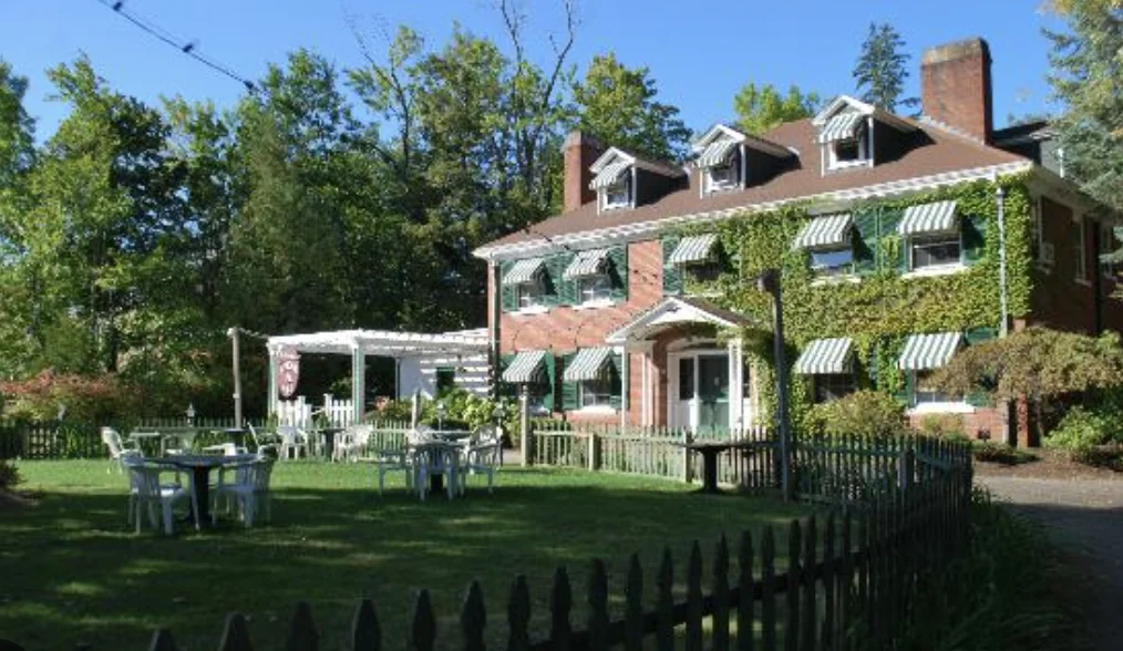 The Governor's Inn in high summer, the ivy-covered brick estate with green striped awnings above the lawn, pergola, and picket fence