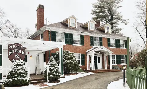 The Governor's Inn in falling snow, the brick manor with green shutters, the white pergola, and the Spaulding Steak & Ale sign