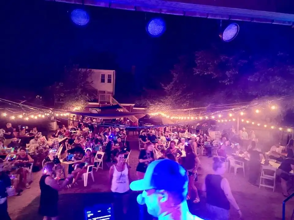 A full crowd under the string lights at The Garage beer garden at night, seen from the stage