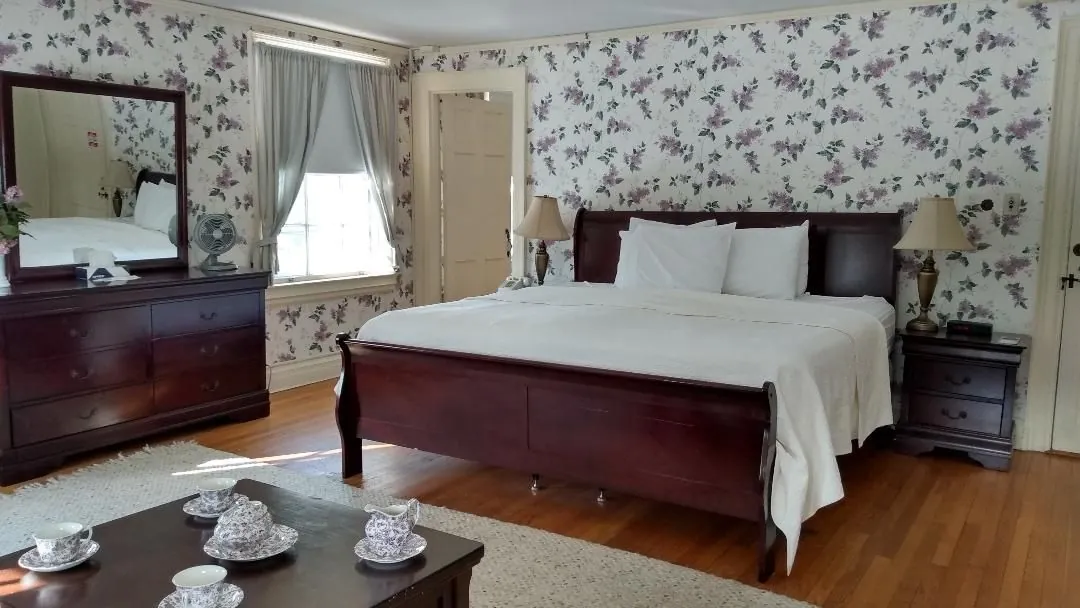 A guest room at The Governor's Inn, mahogany sleigh bed, lilac wallpaper, and morning light on the original wood floors