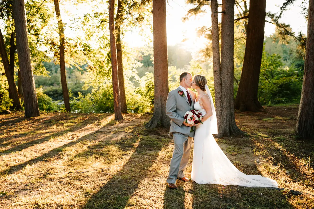 A bride and groom kissing in golden evening light beneath the pines on the Spaulding estate